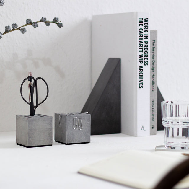 Eine Büroszene präsentiert einen Stiftehalter, einen Büroklammernhalter aus Beton und zwei Buchstützen, die jeweils zwei Bücher auf einem Schreibtisch halten