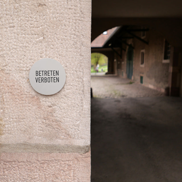 Rundes Betonschild an einer Hauswand mit der Aufschrift BETRETEN VERBOTEN