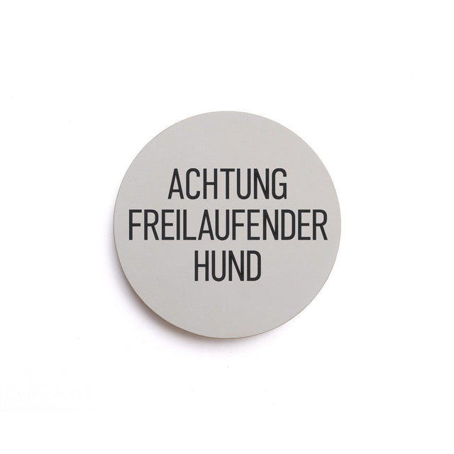 Hinweisschild aus Beton mit dem Text: ACHTUNG FREILAUFENDER HUND