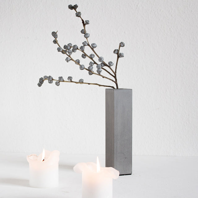 Minimalistische Betonvase, ergänzt durch Kerzen und einen Ast als Dekoration