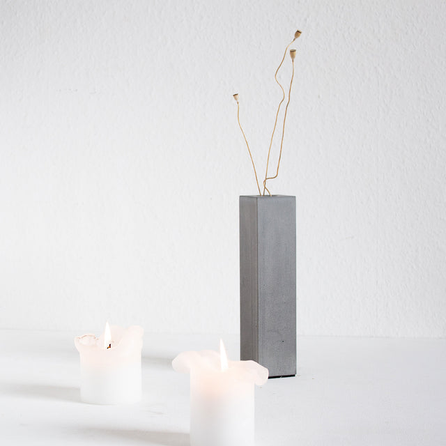 Minimalistische Betonvase, ergänzt durch zwei Kerzen und einen Zweig als Dekoration