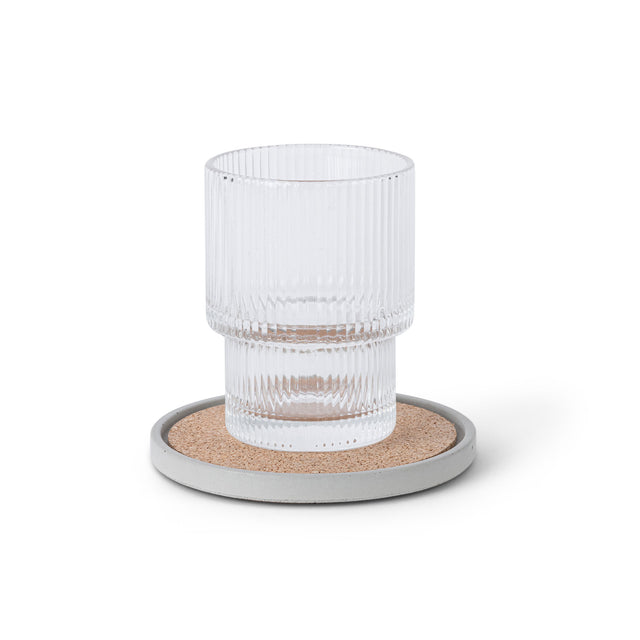 Geriffeltes Glas auf rundem Beton-Untersetzer in Hellgrau mit Korkeinlage