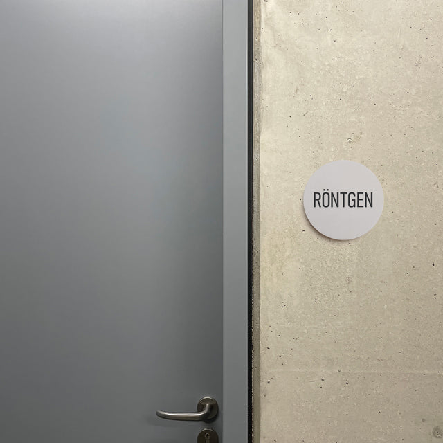 Rundes Schild aus Beton an einer Wand mit dem Text RÖNTGEN