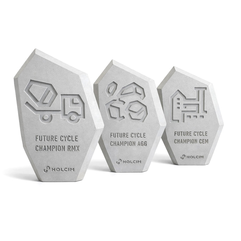 Drei polygonale Awards aus hellem Beton mit reliefartigen Motiven und eingeprägter „Future Cycle Champion“-Beschriftung sowie Holcim-Logo