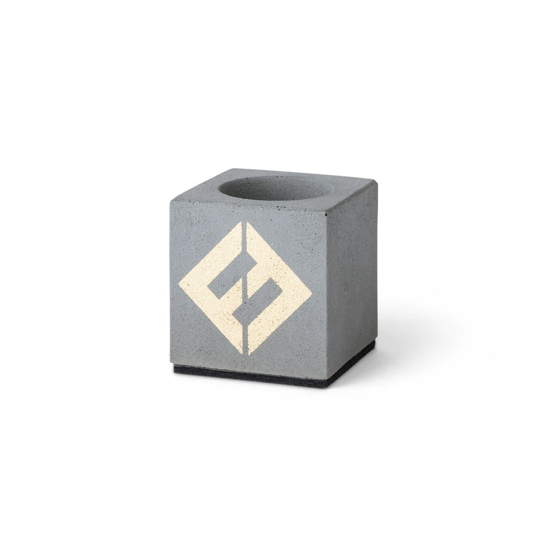 Ein stilvoller Teelichthalter aus Beton, dessen kubische Form mit einem goldenen Logo veredelt ist