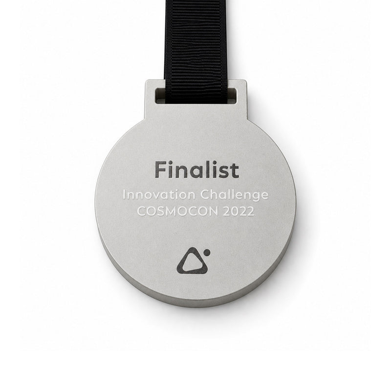 Runde Betonmedaille in Hellgrau mit schwarzem Textilband – bedruckt mit „Finalist, Innovation Challenge COSMOCON 2022" und dem COSMOCON-Logo per UV-Direktdruck.