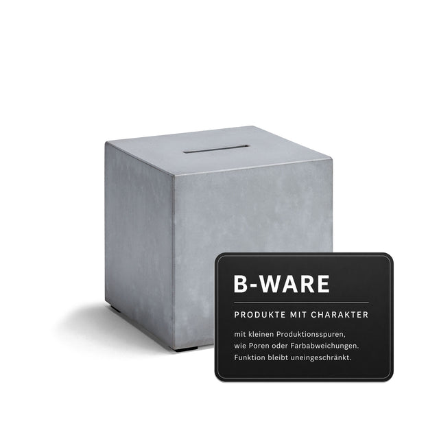 Quadratische Beton-Spardose mit Schlitz oben auf weißem Hintergrund, daneben Hinweis „B-WARE – Produkte mit Charakter“ mit Beschreibung zu kleinen Produktionsspuren.